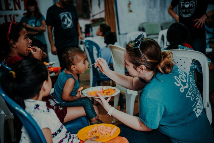 a woman feeding a plate of food to children